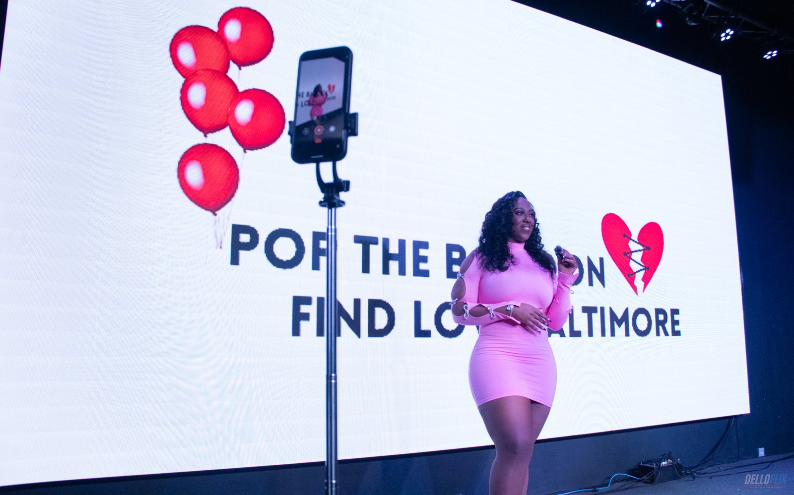 A host filmed on a phone rig in front of the LED wall during a live show