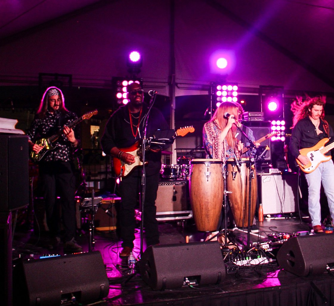 An outdoor tented stage with lighting and sound, set up for a live band